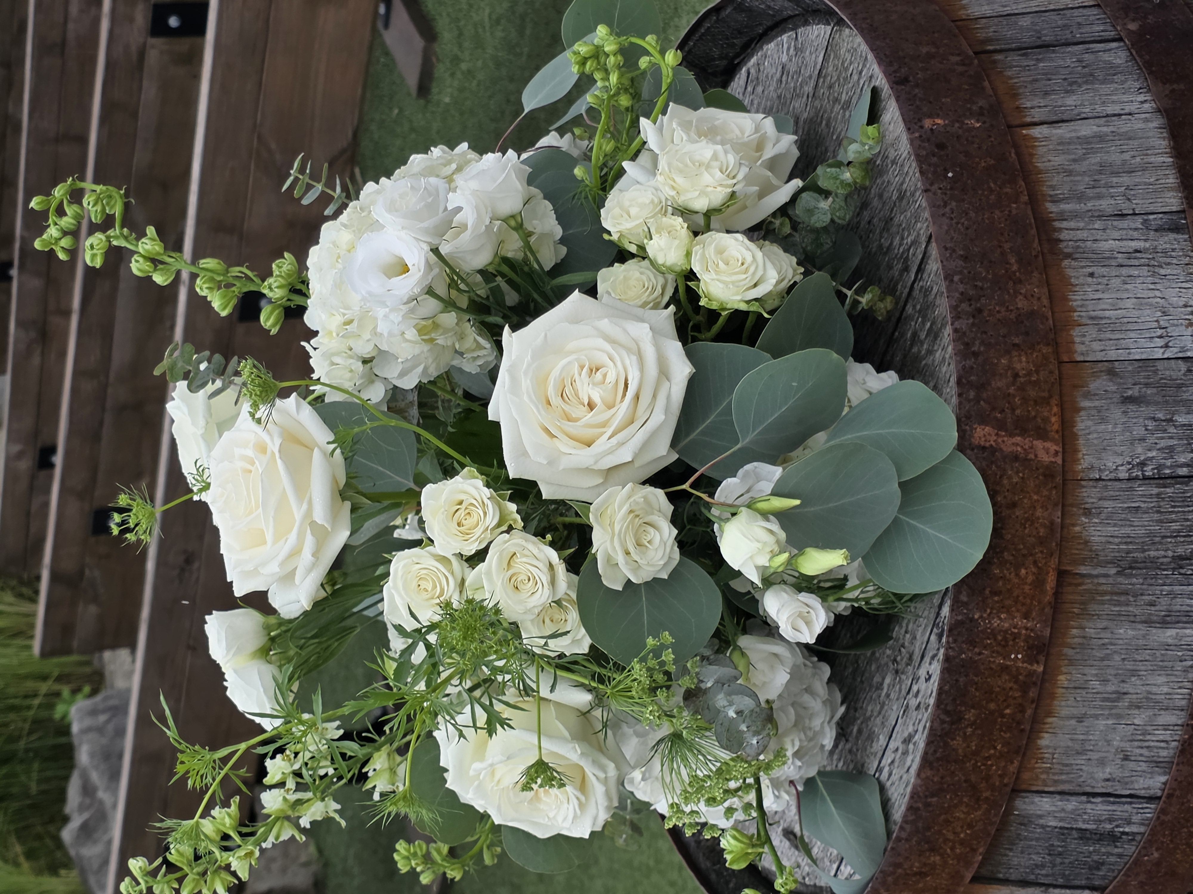 White roses and delicate seasonal flowers with eucalyptus at an outdoor wedding