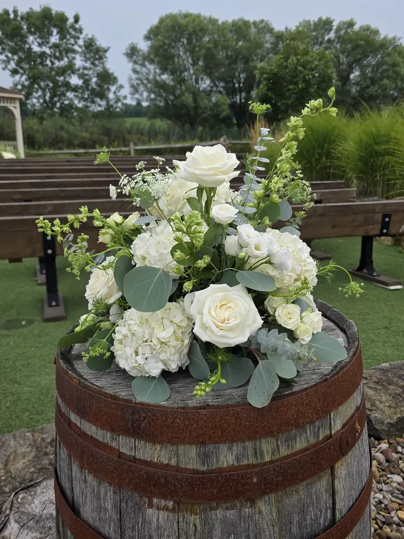 White roses and hydrangeas with eucalyptus arranged on a wooden barrel at an outdoor ceremony