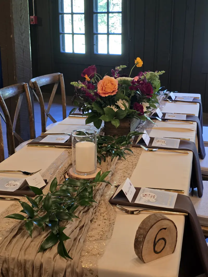 A reception table with orange and burgundy flowers, candles, and trailing greenery