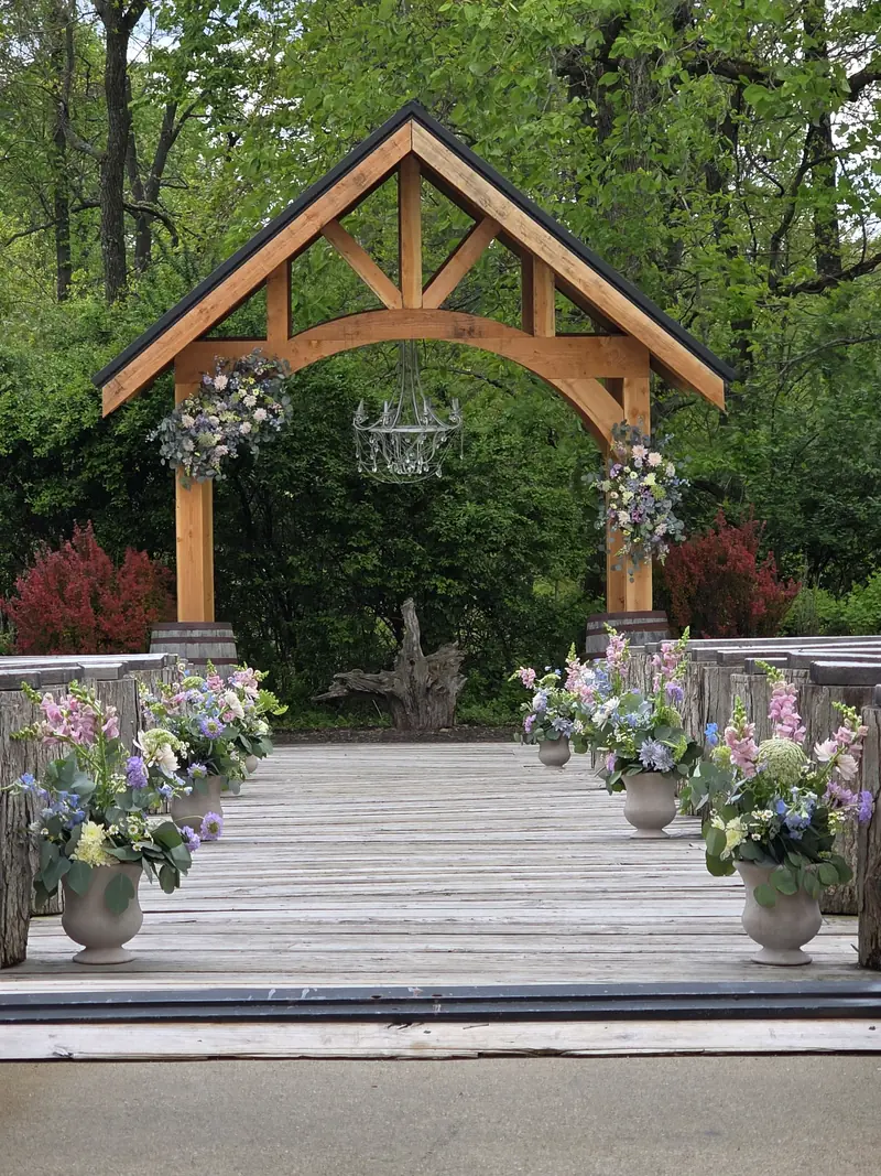 A flower-lined outdoor wedding aisle leading to a wooden arch in a green garden