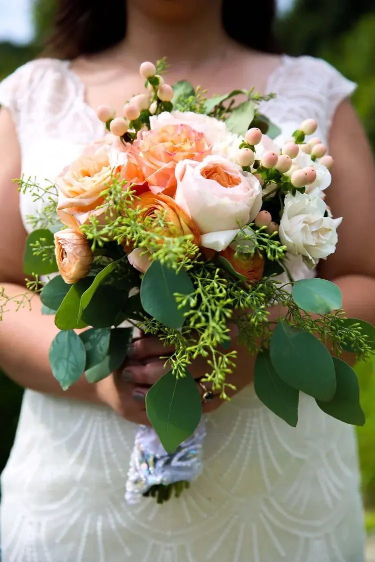 A bride holding a peach and blush rose bouquet with trailing eucalyptus